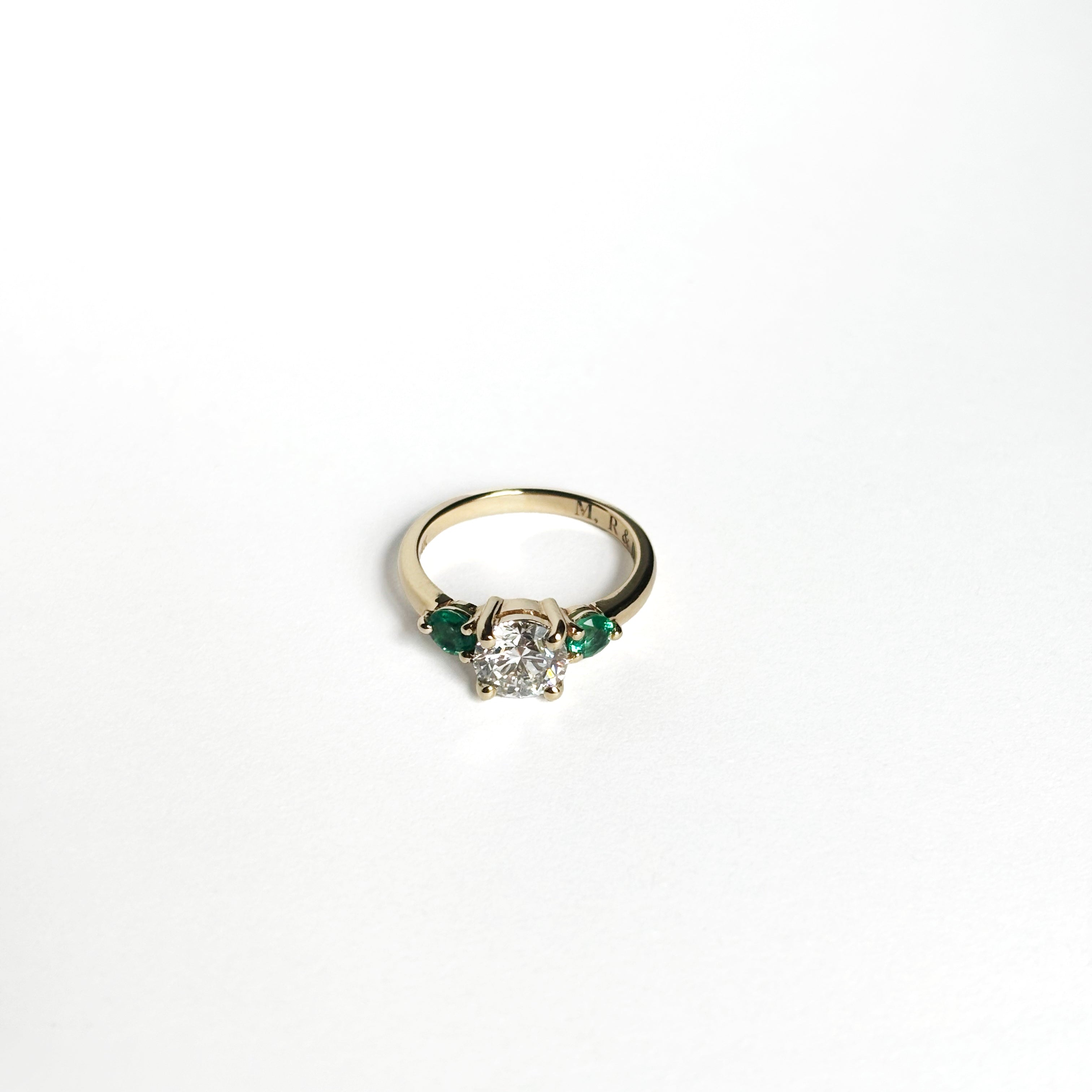Round diamond ring with emerald side stones